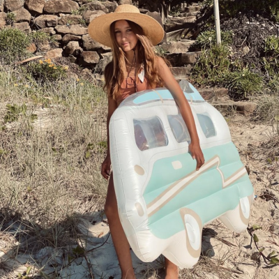 Flutuador insuflável com design de carrinha azul claro e branca, mulher com chapéu de palha na praia