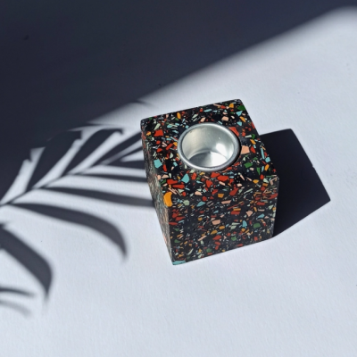 Castiçal quadrado colorido com padrão de azulejos em fundo branco e sombra de planta.