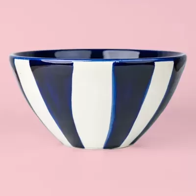 Taça azul e branca com padrão de listras verticais em fundo rosa