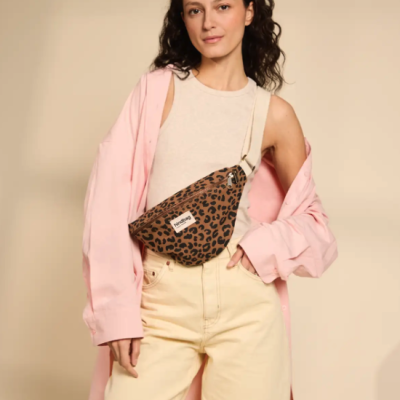mulher com t-shirt cinza claro, camisa rosa e calças creme usando mochila tipo pochete com padrão leopardo
