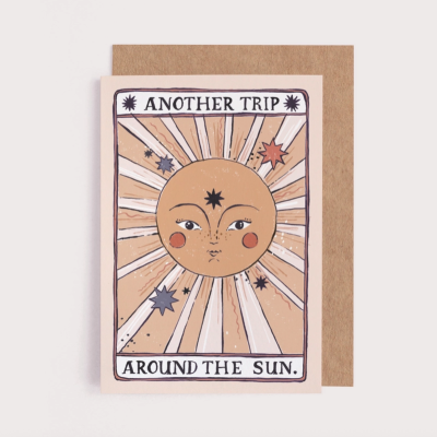 Cartão ilustrado com rosto do sol e texto decorativo acompanhado de envelope castanho