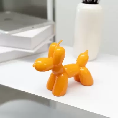 Estatueta de cachorro balão laranja sobre mesa branca com vaso branco e caixas ao fundo