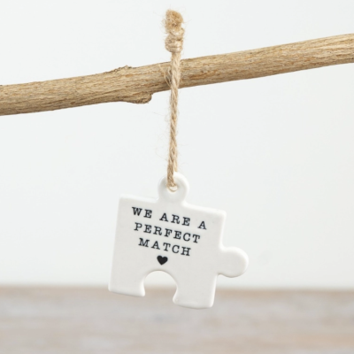 Peça de puzzle cerâmica branca com cordão de juta e texto impresso pendurada num ramo