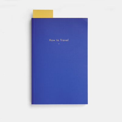 Livro azul com texto How to Travel e marcador amarelo