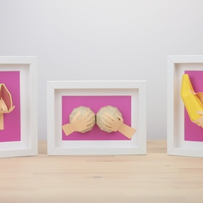Três quadros com esculturas 3D de mãos em papel a segurar fruta e bolachas, fundo rosa