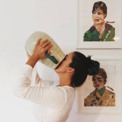 Pessoa a beber de uma caneca cerâmica grande com relevos, com dois quadros artísticos na parede
