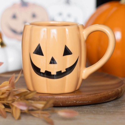 Caneca de cerâmica laranja com rosto de abóbora de Halloween em base de madeira.