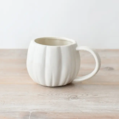 Caneca de cerâmica branca com textura ondulada sobre mesa de madeira clara