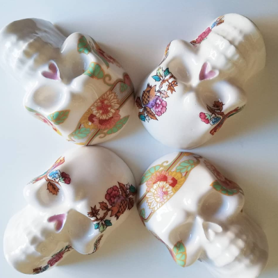 Quatro caveiras de cerâmica branca com padrões florais coloridos e corações cor de rosa nas têmporas