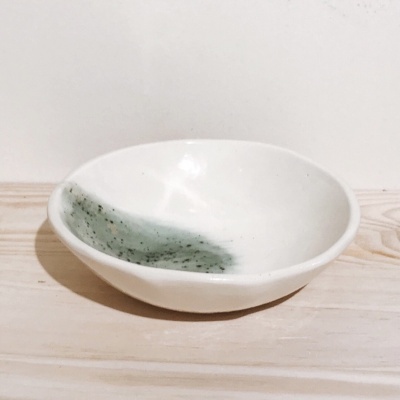 Prato raso branco com detalhe verde e manchas pretas em cerâmica sobre madeira clara