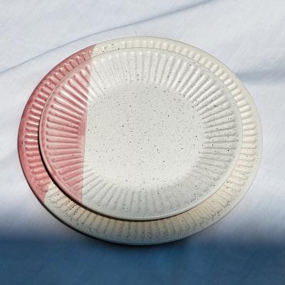Dois pratos redondos de cerâmica texturizados, um creme com manchas e meio rosa, outra creme, sobre tecido azul claro.