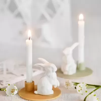 Duas castiçais com velas e figuras de coelhos brancos sobre mesa com flores
