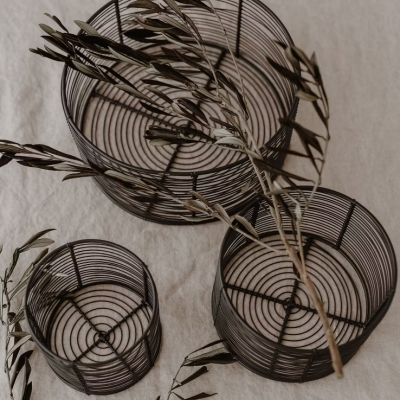 Três cestos de arame pretos com padrão circular, tecido claro e galhos secos