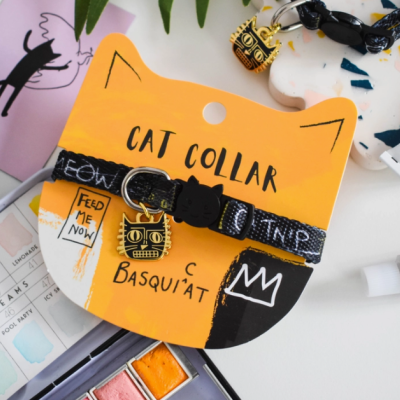 Colar preto para gato com padrão branco e pendente dourado em embalagem amarela com texto