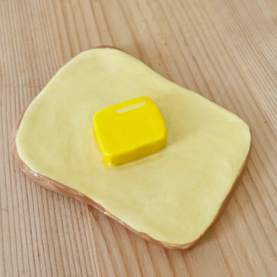 Figura decorativa de cerâmica simulando pão com manteiga sobre madeira clara