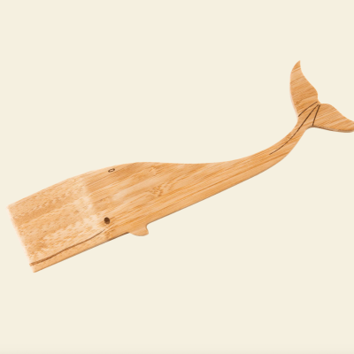 Prancha de madeira em forma de baleia sobre fundo bege claro