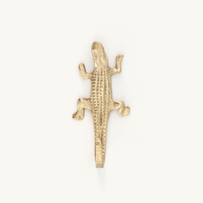Acessório dourado em forma de crocodilo sobre fundo branco.