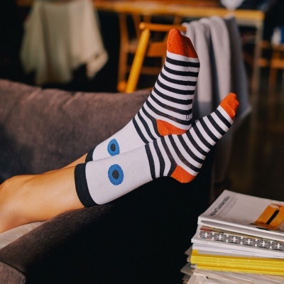 Meias riscas pretas e brancas com detalhes laranja e olhos azuis em uma pessoa no sofá