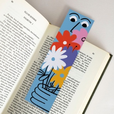 Marcador de livros colorido com desenho de mão azul segurando flores sobre livro aberto