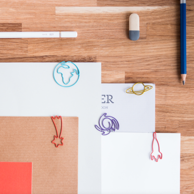 Clips de papel com formas de planetas e foguete em folhas sobre mesa de madeira com material de escrita