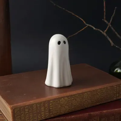 Figura decorativa de fantasma em cerâmica branca com olhos pretos sobre livros antigos