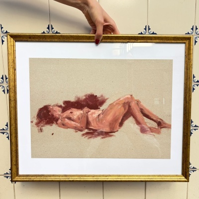 Pintura de figura humana reclinada em moldura dourada segura por mão com unhas vermelhas, fundo de azulejos brancos com padrão azul