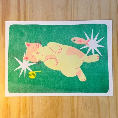 Ilustração de gato amarelo com manchas rosa, duas estrelas brancas, uma bolinha amarela e um peixe cor-de-rosa sobre fundo verde