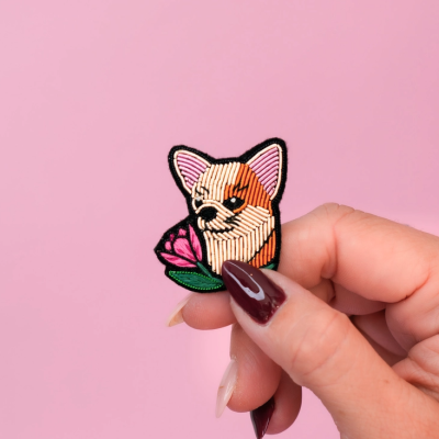 Patch bordado de cabeça de cão com flor, segurado por mão feminina.