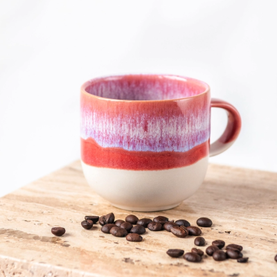 Caneca cerâmica colorida e grãos de café sobre pedra clara