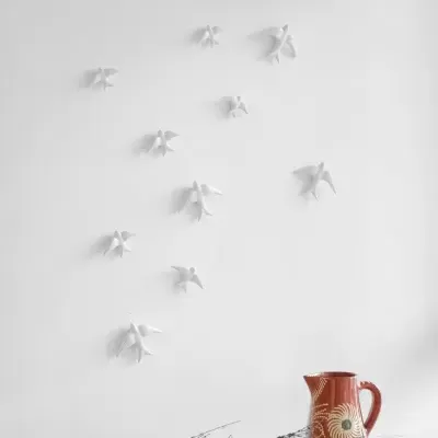 Jarro vermelho decorativo, cesta com ramos secos e aves brancas em relevo na parede