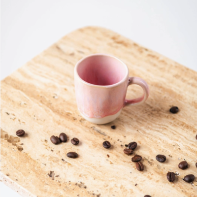 Caneca de cerâmica rosa numa superfície de pedra bege com grãos de café
