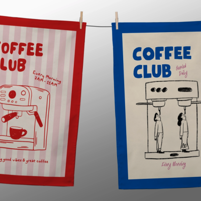 Dois panos de cozinha com ilustrações e texto relacionados a café, um vermelho e outro azul, pendurados com molas numa corda.