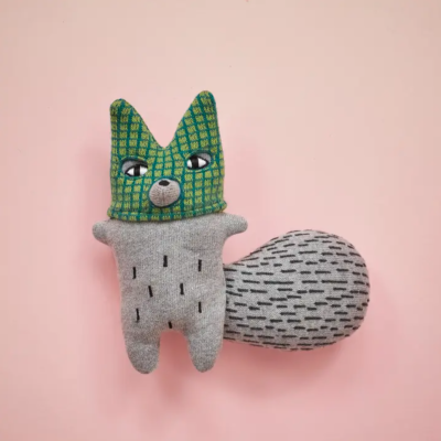 Pelúcia tipo animal com cabeça verde quadriculada e corpo cinzento com padrão preto
