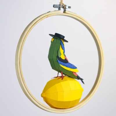 Pássaro em origami colorido com chapéu preto sobre limão amarelo em origami dentro de anel de madeira