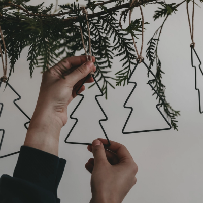 Mãos penduram ornamentos em forma de árvore de Natal de metal preto com cordão numa árvore verde