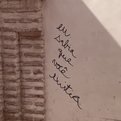 Parede branca com escrita manuscrita preta e estrutura de tijolos à esquerda