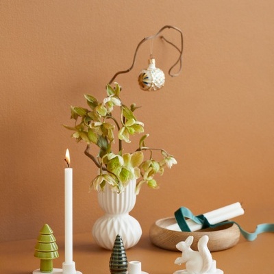 Castiçais, vaso decorativo com folhagem e ornamentos natalícios sobre fundo castanho