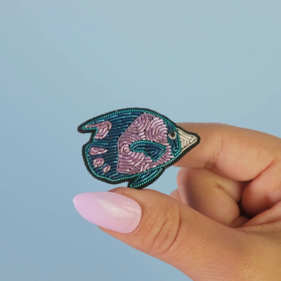 Broche peixe azul e rosa segurado por mão com unhas cor-de-rosa