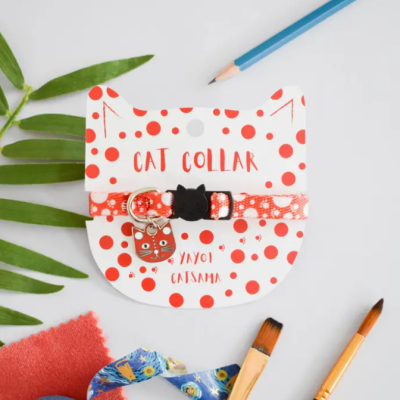 Coleira para gato vermelha com pontos brancos e pendente, em suporte com padrão de pontos vermelhos e texto em fundo branco.