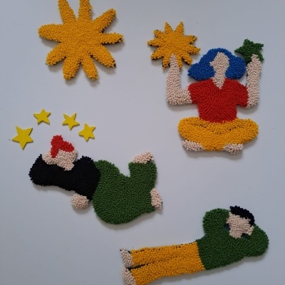 Figuras decorativas felpudas coloridas representando sol, mulher com estrelas e lua, homem com gorro vermelho e homem de camisa verde.