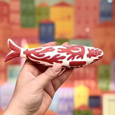 Escultura de peixe branca e vermelha segurada por uma mão com fundo colorido desfocado