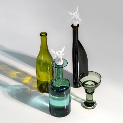 Quatro peças de vidro verde e transparente com tampas decorativas brancas e um copo, sobre fundo claro