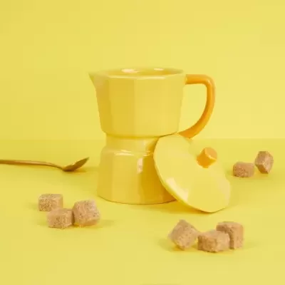 Cafeteira amarela com tampa e cubos de açúcar castanho num fundo amarelo