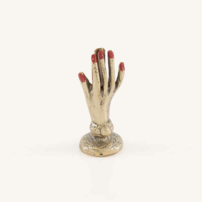 Escultura de mão dourada com unhas vermelhas em fundo branco