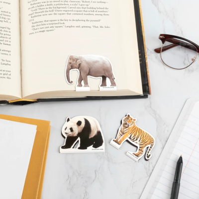 Marcadores de livros em forma de elefante, panda e tigre sobre mesa com livro, óculos e cadernos