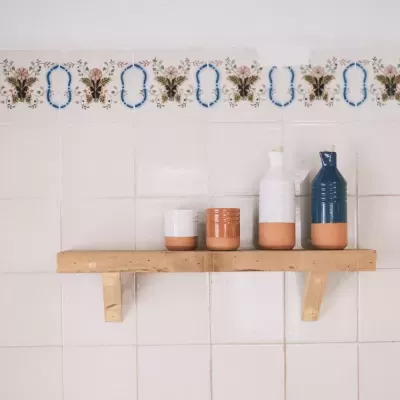 Prateleira de madeira com três recipientes cerâmicos em parede de azulejos brancos decorados
