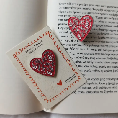 Pins em forma de coração vermelho com padrão floral branco sobre cartão e livro aberto