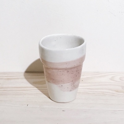 Copo de cerâmica branco com faixa cor-de-rosa sobre mesa de madeira clara