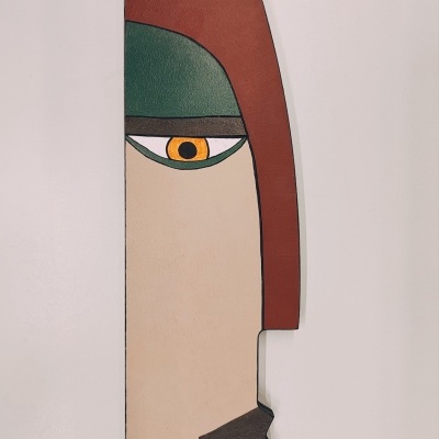 Escultura vertical colorida de rosto humano estilizado em parede branca