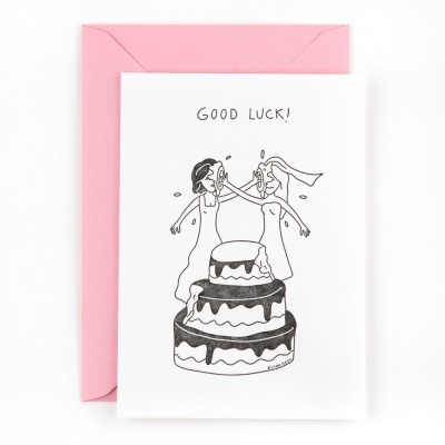 Cartão branco com ilustração de noivos e bolo de casamento, texto 'GOOD LUCK!', e envelope rosa